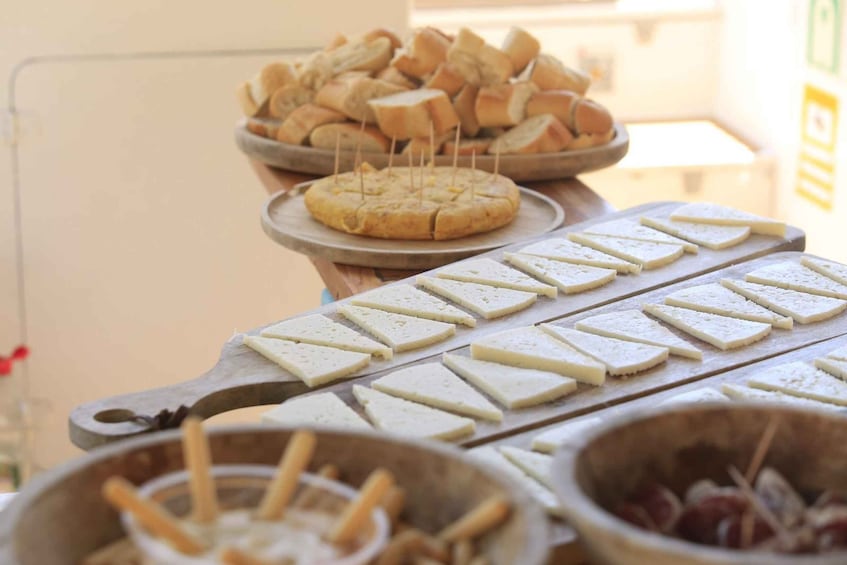 A wooden board with cheese slices, a bowl of breadsticks, and a plate of bread. 3