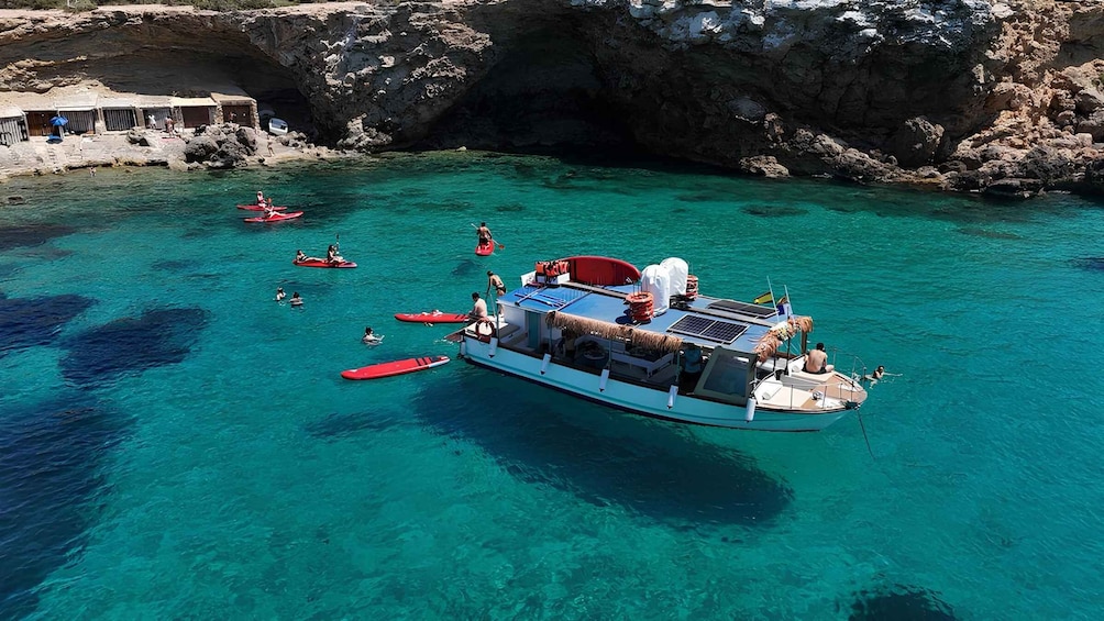 A boat with people kayaking in clear turquoise waters near rocky cliffs. 1