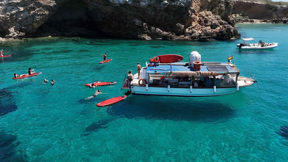 A boat with people on red paddleboards in clear turquoise waters near rocky cliffs. 2
