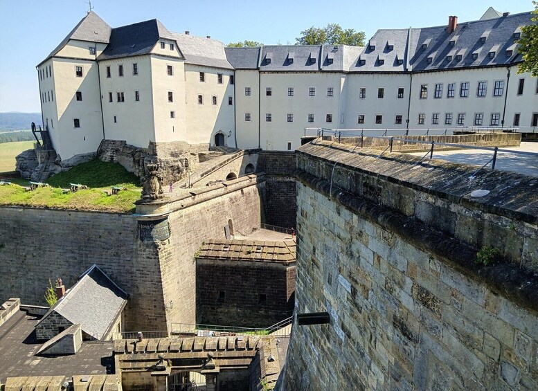 A historic castle with a fortified wall and a large building with multiple windows. 1