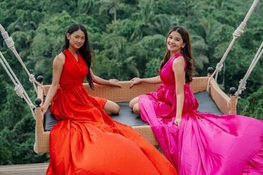 Dos mujeres con vestidos coloridos sentadas en una mecedora de mimbre con un fondo verde exuberante. 3