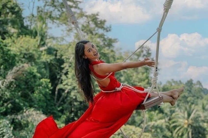 Una persona con un vestido rojo en un columpio, rodeada de vegetación exuberante. 4