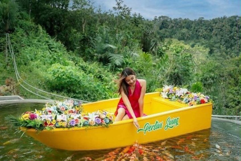 Une femme vêtue d’une robe rouge est assise dans un bateau jaune décoré de fleurs, entourée d’une végétation luxuriante. 2