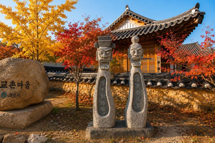 A traditional Korean building with a tiled roof, surrounded by autumn foliage and stone statues. 5