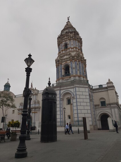A historic building with a bell tower, a street lamp, and a fountain. 1