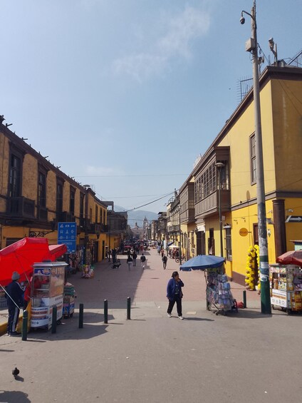 A bustling street with yellow buildings, people walking, and street vendors. 3