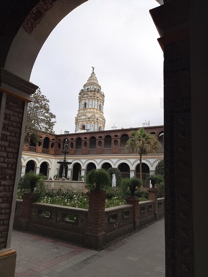 A historic building with a tower, arched walkways, and a garden with trimmed bushes. 2