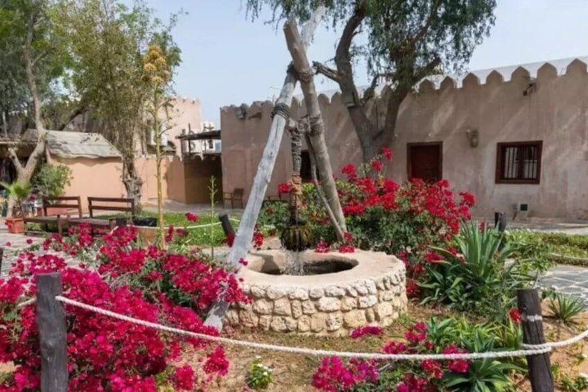 A garden with a stone well, pink bougainvillea flowers, and a rustic building with a crenellated wall. 3