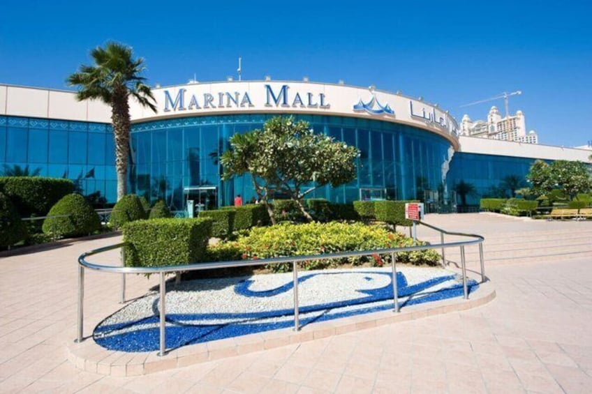 The exterior of Marina Mall with a blue logo, palm trees, and a landscaped area with a circular pattern. 2