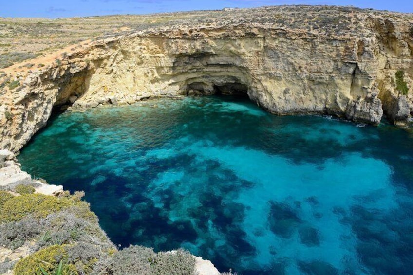 A coastal cliff with a natural cave entrance and clear turquoise waters. 5