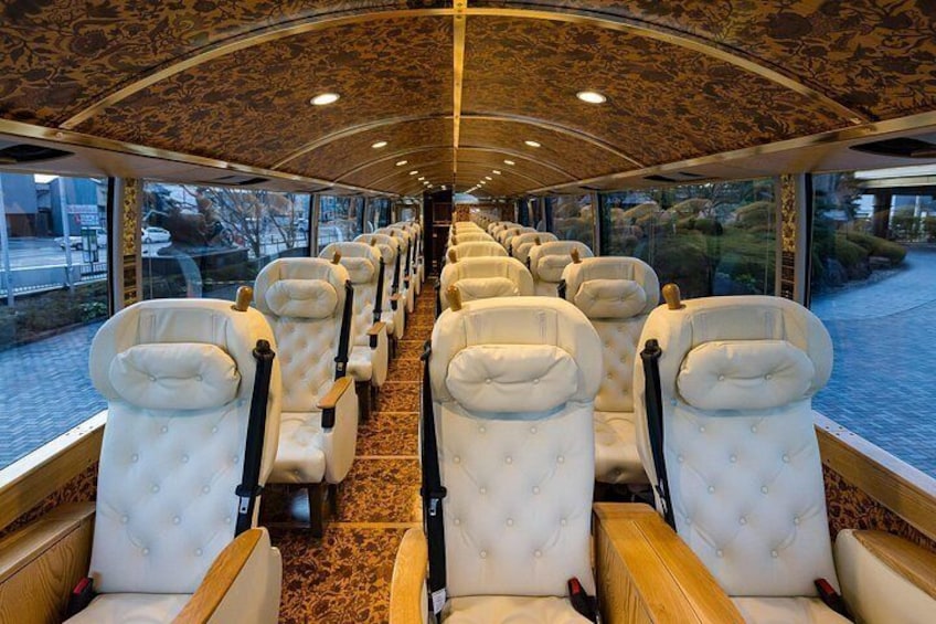A train interior with rows of white upholstered seats, a patterned carpet, and a curved ceiling. 1