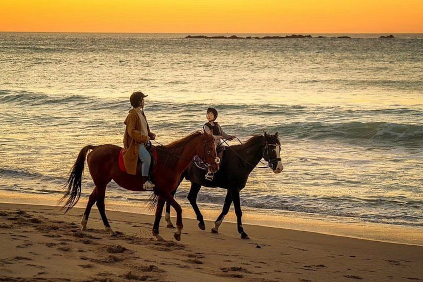 To personer rider på heste langs en strand ved solnedgang. 1