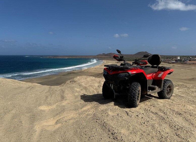 A red ATV parked on a sandy beach with the ocean in the background. 3