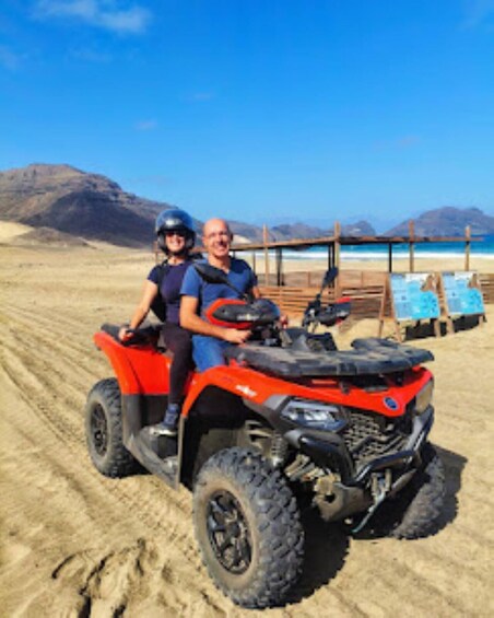 A red ATV on a sandy beach with mountains in the background. 2