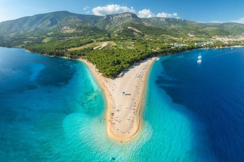 A coastal landscape with a beach, clear turquoise waters, and a mountainous backdrop. 4