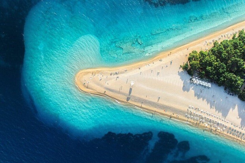 An aerial view of a beach with clear turquoise waters, a sandy shore, and a small cluster of trees. 3