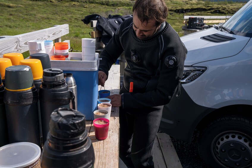 A person preparing food on a wooden table with various containers and a car nearby. 5