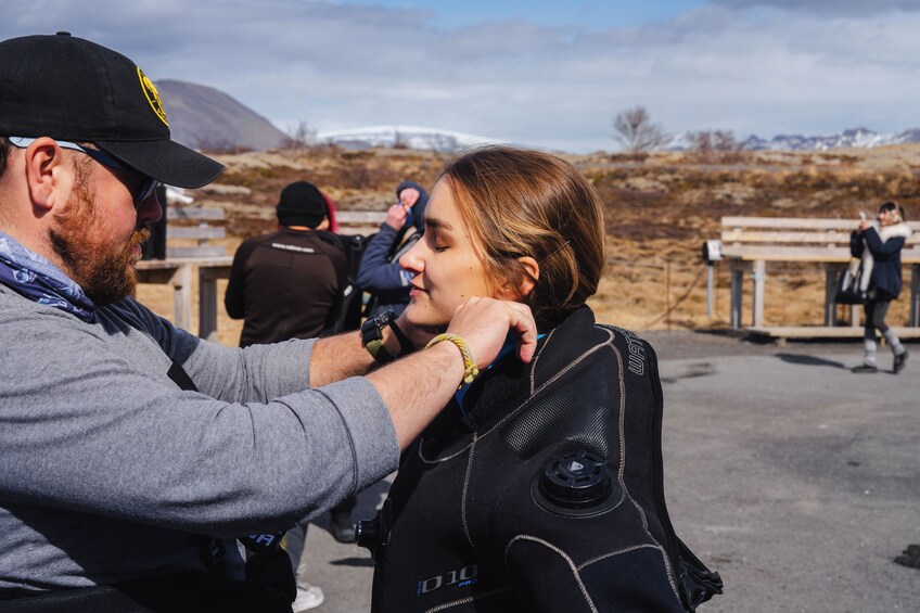 A person wearing a black jacket with a zipper and a name tag, standing outdoors with a mountainous background. 4