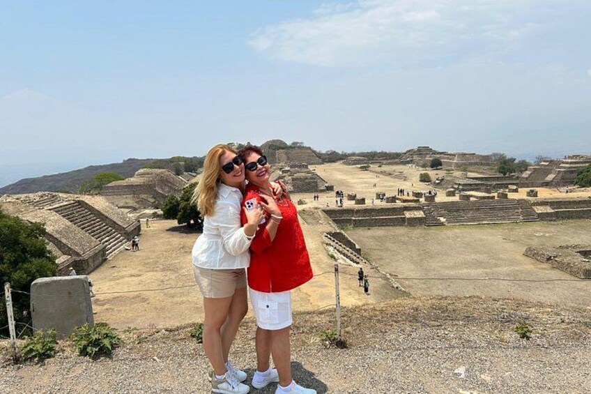 Two people standing on a hill overlooking ancient ruins with stepped structures and a clear sky. 3