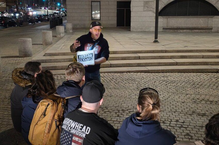 A person speaking to a group of people outdoors at night. 2
