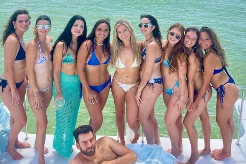 Un grupo de personas en un bote con una cola de sirena, un mar azul cristalino y una zona verde al fondo. 2