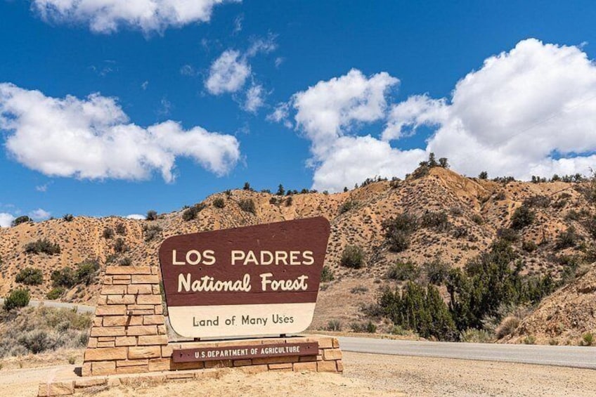 A sign for Los Padres National Forest with a clear sky and a hilly landscape in the background. 4