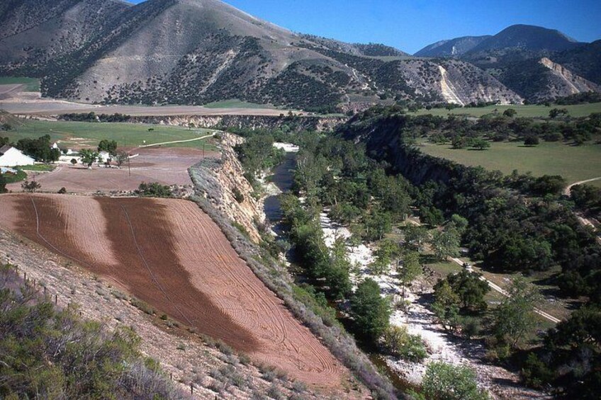 A mountainous landscape with terraced fields, a river, and a small settlement. 2