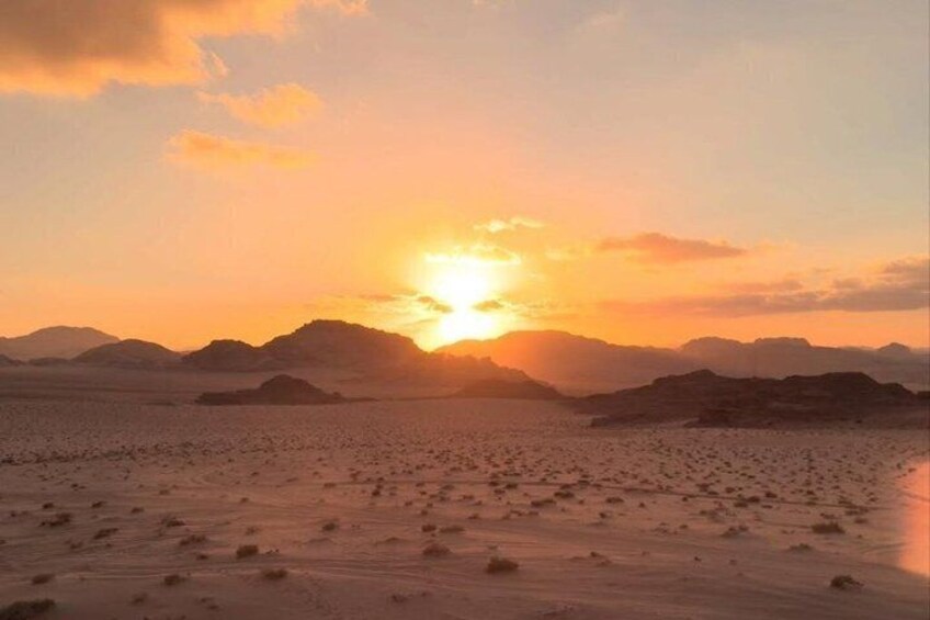 Paisaje desértico con un atardecer, montañas al fondo y un primer plano de arena. 1