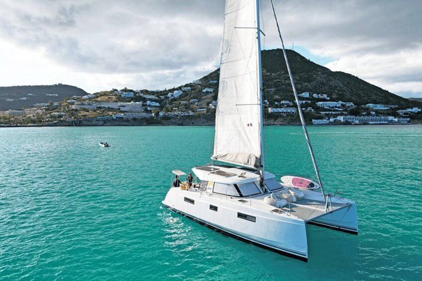 A sailboat on turquoise water with a mountainous coastline in the background. 1