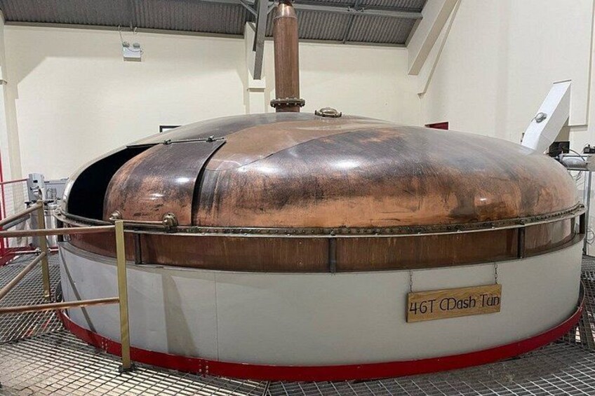Un recipiente de cobre grande con una etiqueta que dice '4GT CDash 1bn' en una instalación con piso metálico y equipo industrial. 2