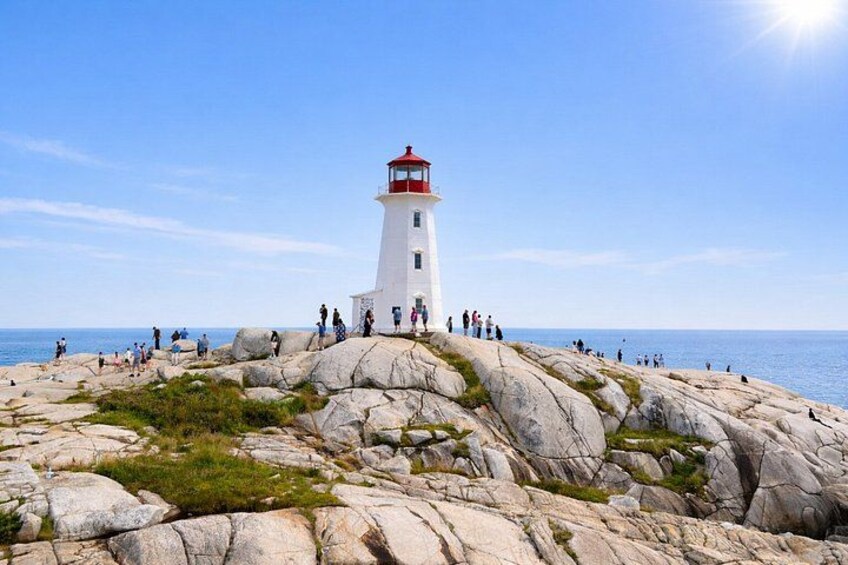 A white lighthouse with a red top on rocky terrain by the sea. 1