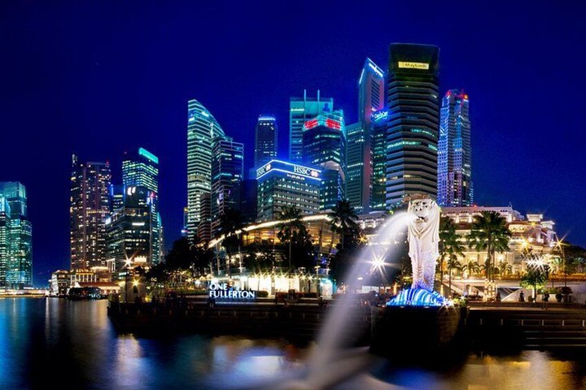 A city skyline at night with illuminated buildings and a statue in the foreground. 2