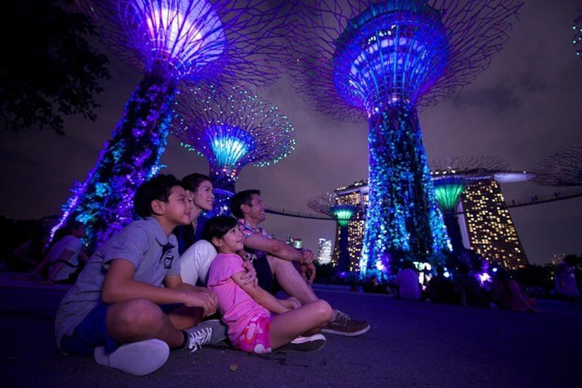 A group of people sitting on the ground with illuminated structures in the background. 1