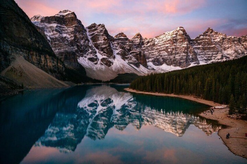 Un lago montano con i riflessi delle cime, circondato da una foresta e montagne innevate. 5