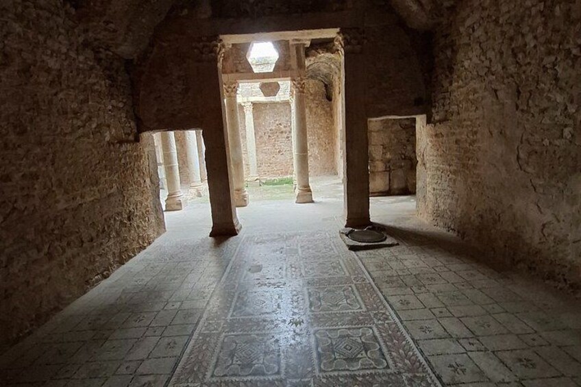 An ancient stone corridor with columns and a patterned floor. 5