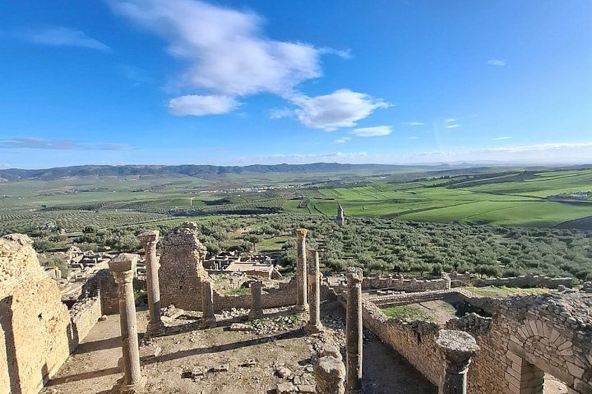 Ancient ruins with columns, surrounded by green fields and distant hills. 2