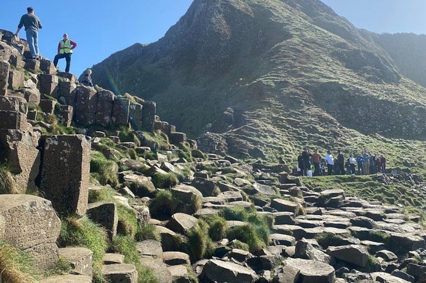 Eine gebirgige Landschaft mit großen Felsen und einer Gruppe von Menschen, die auf einer felsigen Klippe stehen. 1