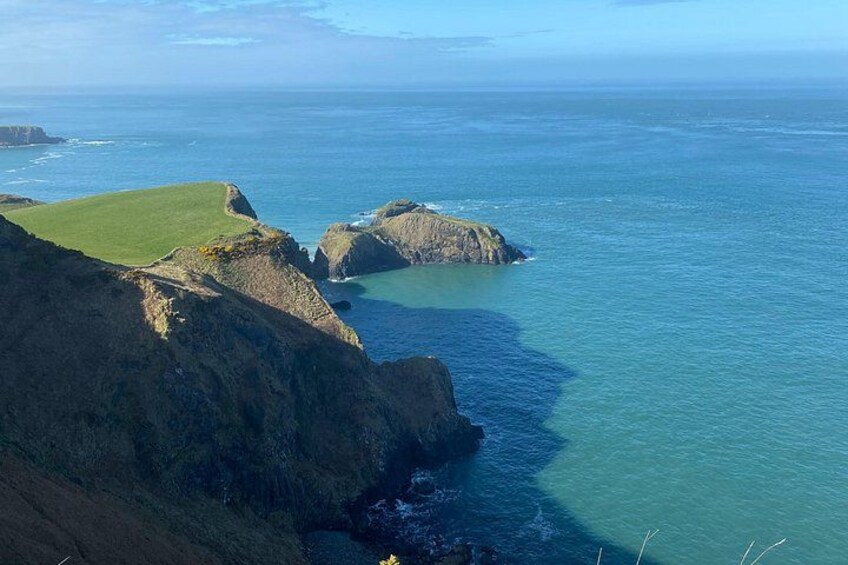 Eine Küstenlandschaft mit Klippen, einer Wiese und dem Meer. 3