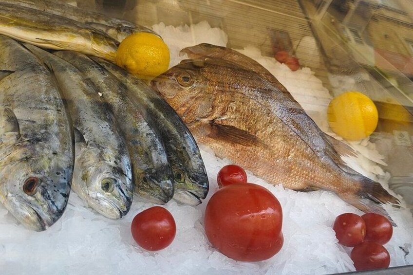 On peut y voir différents types de poissons frais, présentés sur de la glace, notamment un poisson entier et plusieurs filets, accompagnés de citrons et de tomates. 2