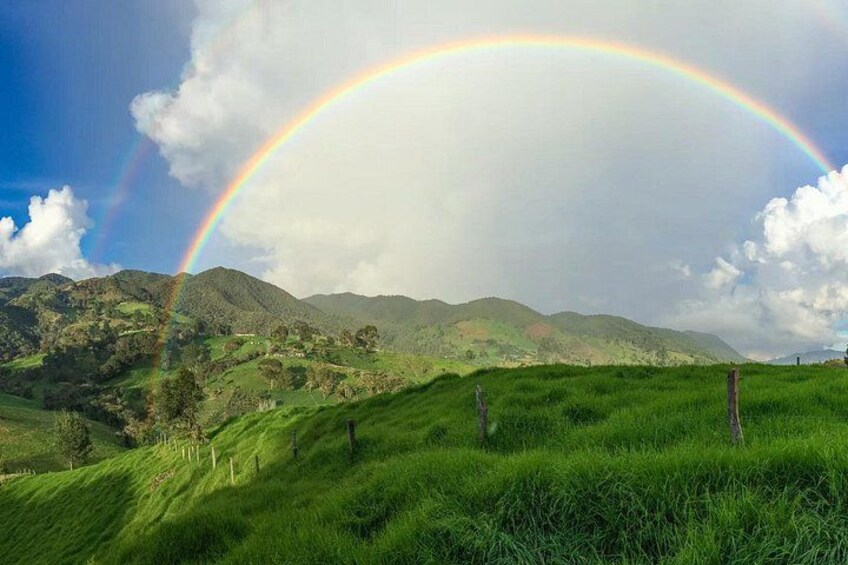 Een weelderig groen landschap met glooiende heuvels en een regenboog die over de hemel boogt. 2