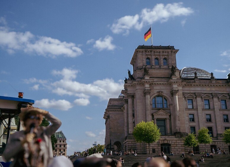 A large historic building with a flag, a dome, and a crowd of people. 4