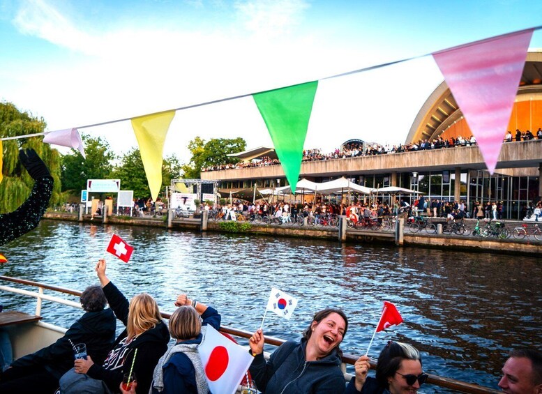 A river with people on a boat, a building with a curved facade, and flags. 3