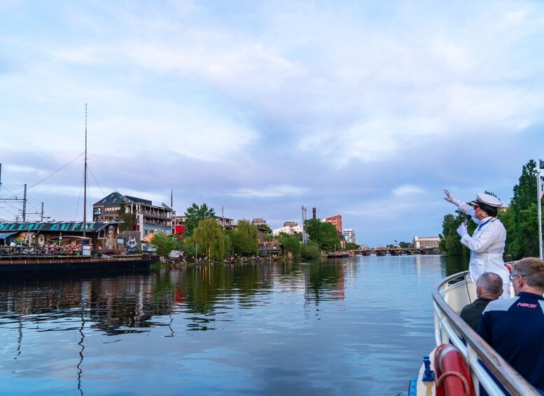 A river with a boat, buildings, and a person in uniform on the shore. 5