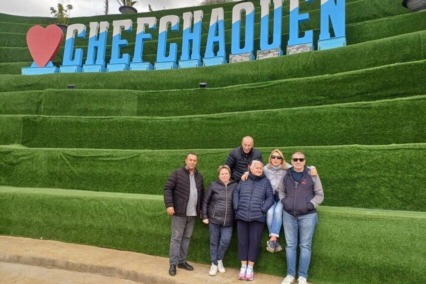 Eine Gruppe von Menschen posiert vor einem Schild mit dem Text 'CHEECHAQUEN' und einem Herzsymbol. 5