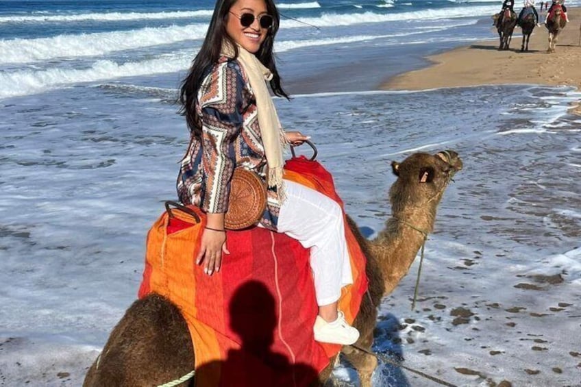 Una persona montando un camello en una playa, con olas de fondo. 1