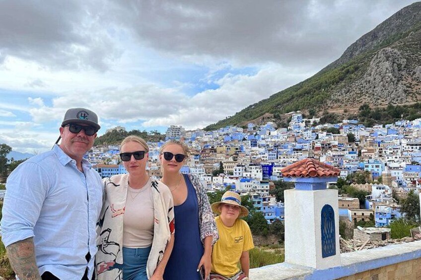Una familia de cuatro personas frente a un pueblo con edificios blancos y una montaña al fondo. 4