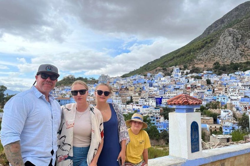 En familie på fire står foran en by med hvide bygninger og et bjerg i baggrunden. 4