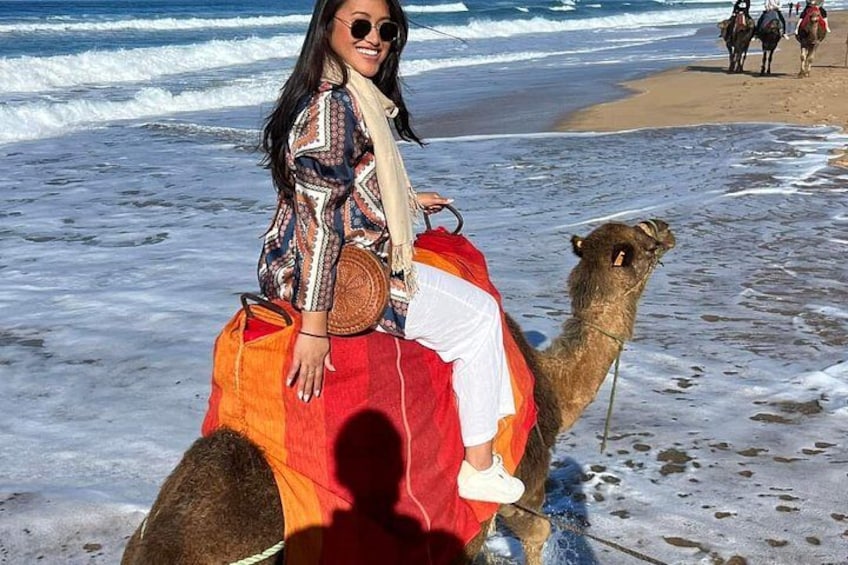 Una persona montando un camello en una playa, con olas al fondo. 1