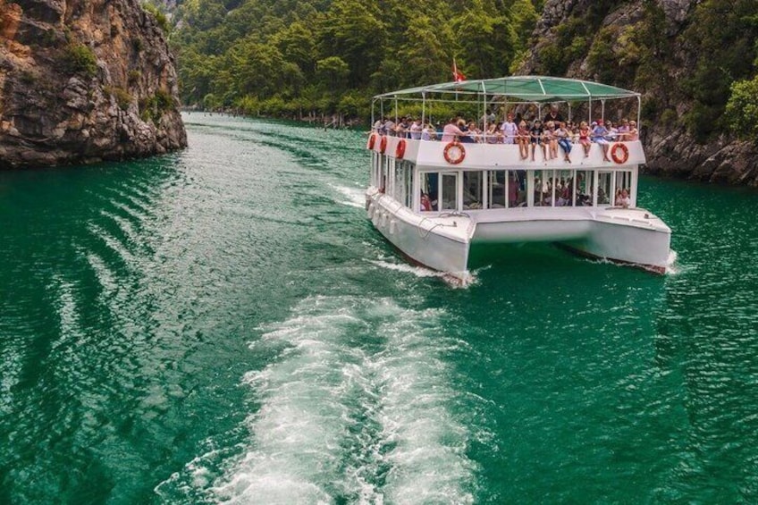 Een boot met passagiers op een turquoise rivier, omgeven door rotsachtige kliffen. 5
