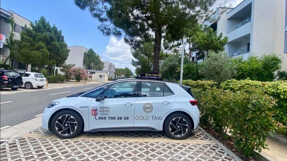 Un taxi bianco parcheggiato su un marciapiede, con il cartello 'GOLD TAXI' e il numero di contatto. 3